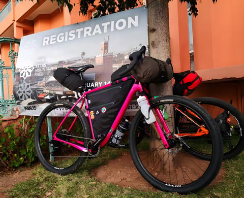 Pink Salsa Cutthroat with bikepacking bags parked by the Atlas Mountain Race registration banner in Marrakech.