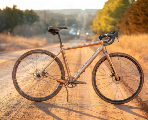 A mud-splattered gold Salsa Stormchaser singlespeed gravel bike stands on an Oklahoma dirt road at sunset.