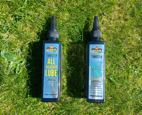 Tru-Tension BananaSlip Tungsten all-weather and wet chain lube bottles side by side on grass.