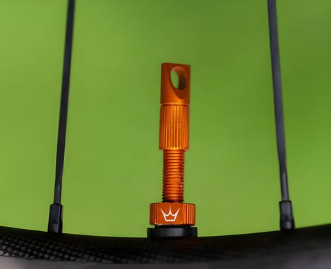 Orange anodised Peaty's tubeless valve fitted to a carbon rim, with wheel spokes either side.