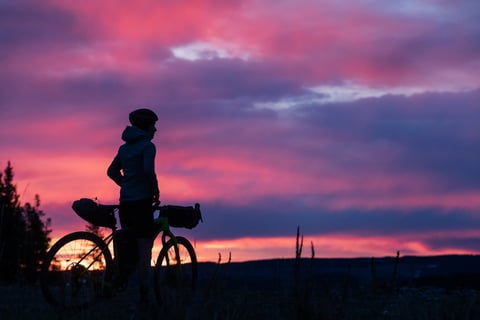 Bikepacker silhouetted beside a loaded bike under a pink dusk sky, from Salsa Cycles' film Choosing to Live.