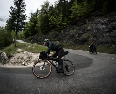 Bikepacker rounds a mountain hairpin road below wooded cliffs with a second rider behind, from the Cycle Touring Festival.