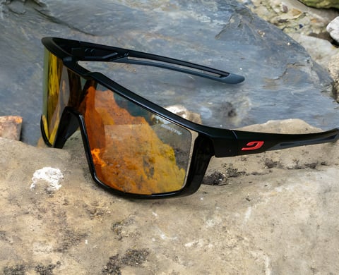 Julbo Fury Reactiv sunglasses with a black frame and orange mirrored photochromic lens resting on rock.