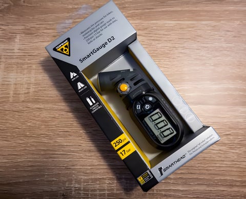 Topeak SmartGauge D2 digital tyre pressure gauge in its retail box on a wooden surface.