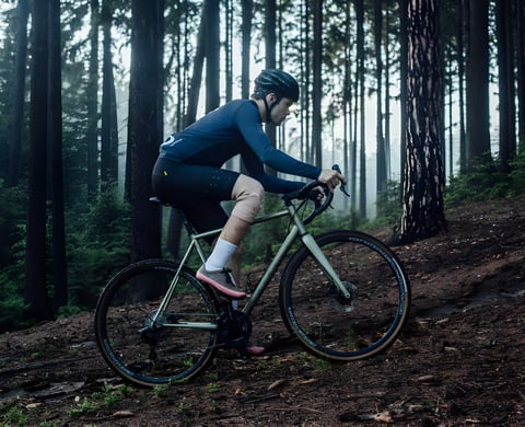 Rider on the Repete Cycles Verne steel gravel bike climbing a dirt track through misty forest.