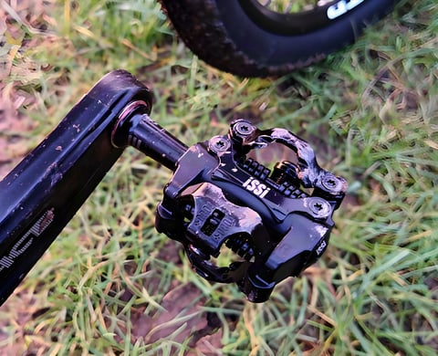 Mud-spattered black iSSi II Triple SPD-compatible pedal fitted to a crank arm, on grass.