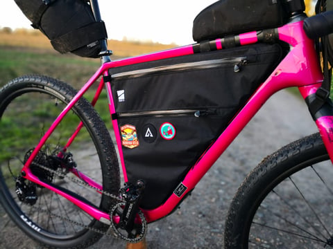 Straight Cut Design custom frame bag with event patches, bolted into the front triangle of a pink Salsa Cutthroat.