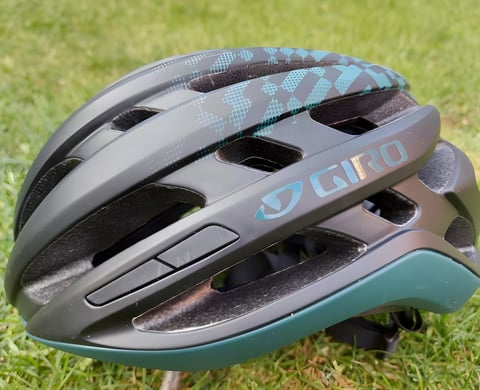 Giro Agilis MIPS helmet in matte black with teal pattern and trim, resting on grass, side view.