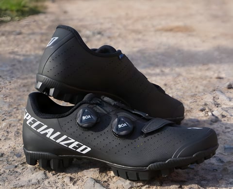 Pair of black Specialized Recon 3.0 gravel shoes with two BOA dials and a velcro strap, resting on a dusty track.