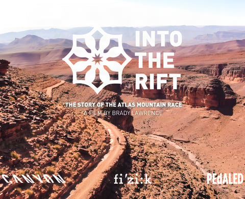 Into the Rift title card for the Atlas Mountain Race film, over a Moroccan canyon track with sponsor logos.