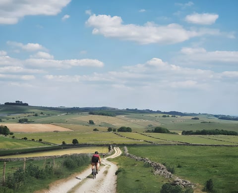 Lone rider on a white gravel track between drystone walls across Peak District fields on the Dirty Kanzelled.