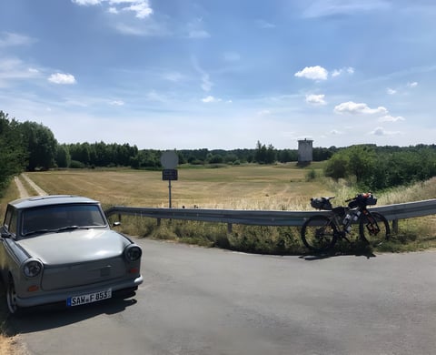 Trabant and loaded bikepacking bike beside a former East German watchtower on the Grenzsteintrophy route.
