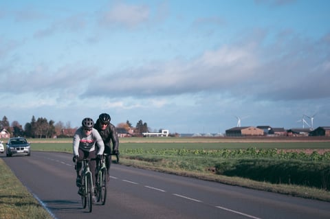 Two riders on Santa Cruz Stigmata road bikes pass flat farmland and wind turbines during the Creepy Fatigue trip in Belgium.