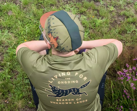 Rider seen from above wears the Cascada Trail Tee with its wolf print and a Stay Wild cycling cap, sitting in heather.