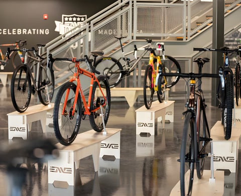 Custom gravel bikes on plywood ENVE stands at the Builder Round-Up 2020, with an orange steel bike at the front.