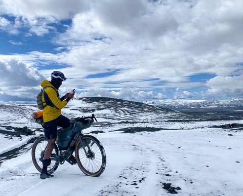 Natt Williams checks his phone astride a loaded Bombtrack Hook on a snowy Iceland Divide track.