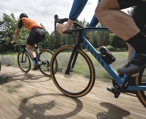 Two riders on Canyon gravel bikes with tan-wall tyres race along a dirt track, promoting the King's Cup gravel festival.