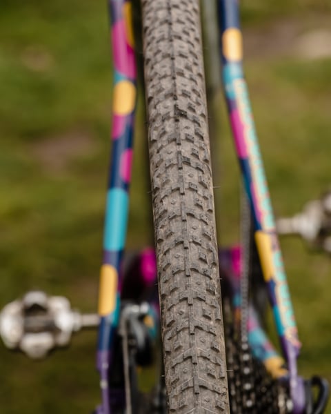 Close-up of a WTB gravel tyre tread between the stays of a colourfully painted gravel bike frame.