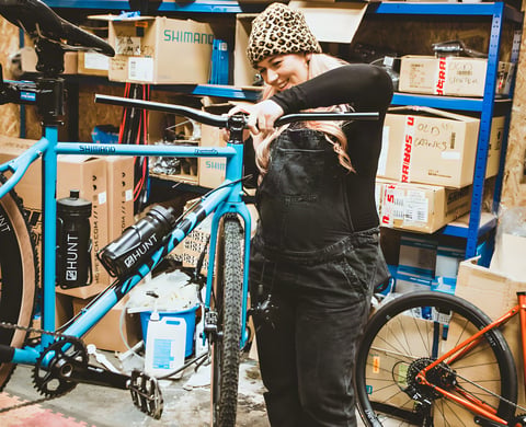Kelly-Jayne smiles as she fits a flat bar to her blue Cotic Escapade in a workshop, 28 weeks pregnant.