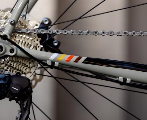 Close-up of the 2021 Bombtrack Audax chainstay in sage green with its stripe decal, cassette and Shimano rear mech.