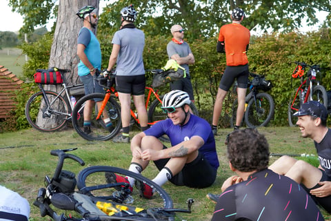Riders chat and rest on the grass beside loaded bikes before the Great British Escapade start.