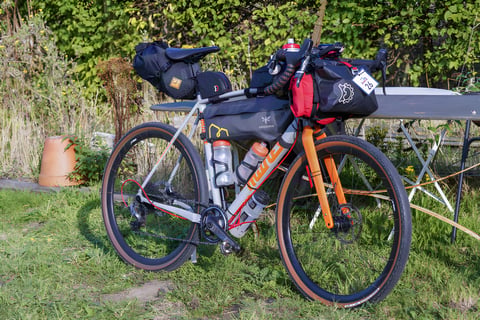 Loaded gravel bike with Apidura frame bag and race number 26, propped against a table at the Great British Escapade start.