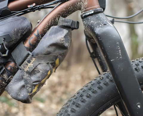 Mud-spattered Apidura Expedition Downtube Pack strapped to the top of the down tube on a Bombtrack Beyond.