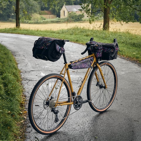 Fairlight Faran build with Wizard Works saddle, frame and basket bags on a wet lane with a church behind.