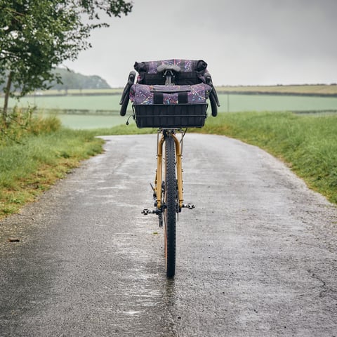 Head-on view of the Wizard Works Faran build, basket bag on the bars, on a wet lane between fields.