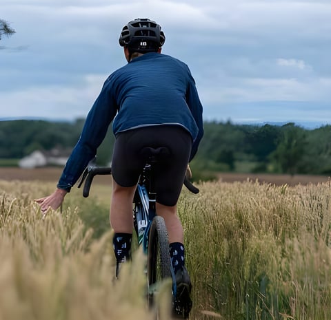 Rider in a navy jacket on a Fustle gravel bike brushes a hand through tall grass in a still from the Graviator film.