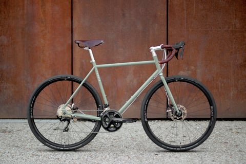 Temple Adventure Disc 2 in pale green with Shimano 105 compact chainset, photographed against a rusty metal wall.