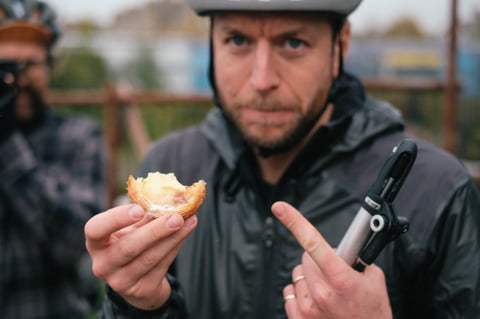Will from Brother Cycles holds up a half-eaten pastel de nata and a mini pump at the Canterbury coffee stop.