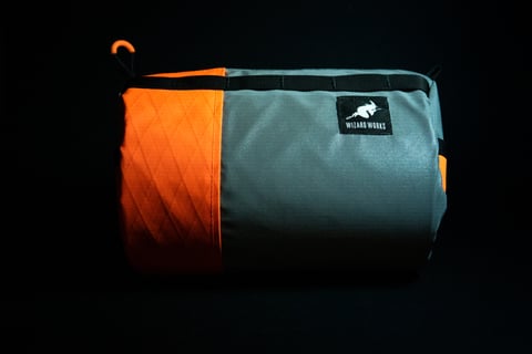 Reflective grey Wiz Viz pouch from above, its black-bound edge and buckle strap lit against a black backdrop.
