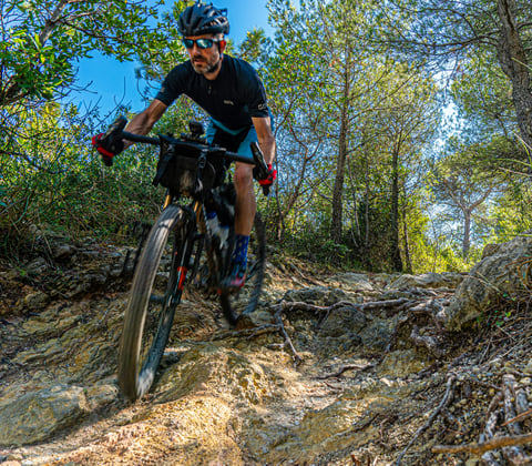Rider on a loaded drop-bar bike fitted with Curve Walmer 55cm handlebars descends a rocky wooded trail.