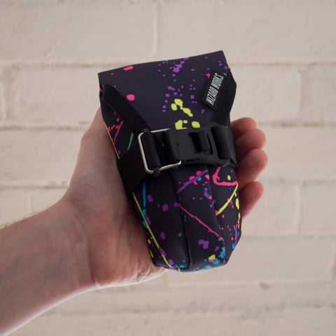 Small Teeny Houdini in the colourful splatter fabric on a dark ground, held in a hand.