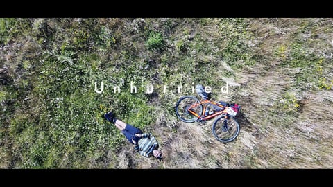 Overhead frame from the film Unhurried: a rider lies in long grass beside a loaded bikepacking bike.