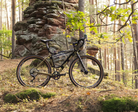 Tout Terrain Vasco gravel bike with frame bag parked beside a red sandstone rock in autumn woodland.