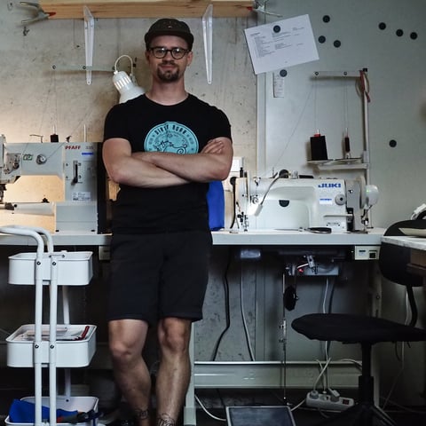Harald of Black Heron Fabrix stands arms crossed between two industrial sewing machines in his Ingolstadt workshop.