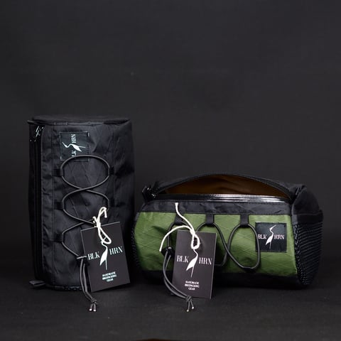 Black Heron Fabrix handlebar bag and cylindrical pouch with bungee cord fronts and hang tags, one black and one olive.