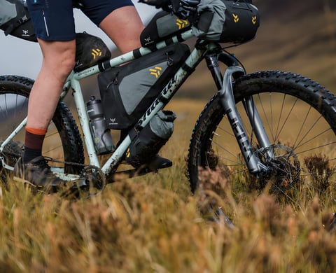 A mountain bike fitted with Apidura Backcountry bags rides through autumn grassland.