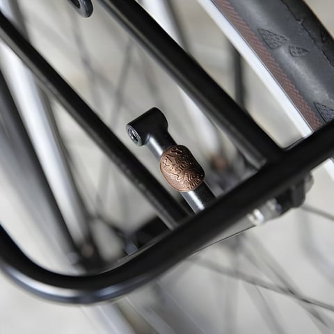 Close-up of a copper Pass and Stow badge on the stay of a black bike rack.