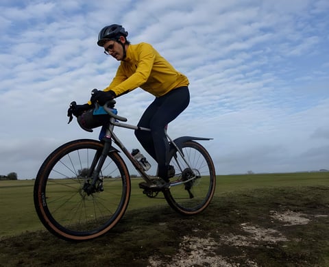 Rider in a yellow Velocio jacket and black tights on a gravel bike on open grassland, testing the Alpha System winter range.