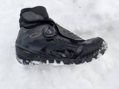 Black Shimano MW7 winter MTB shoe with BOA dial and Gore-Tex logo, resting in fresh snow.