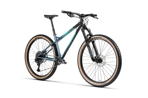 Bombtrack steel Cale in blue-to-teal fade with Maxxis tan-wall tyres, front three-quarter studio view.