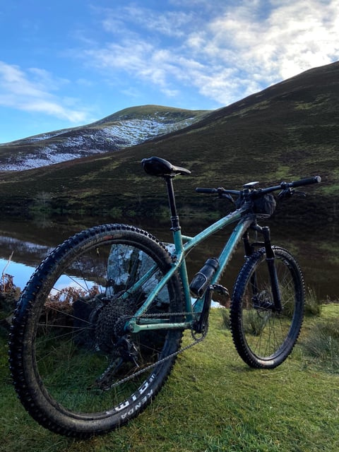 Bombtrack Cale AL hardtail in mint green stands beside a still reservoir below the snow-dusted Pentland Hills.
