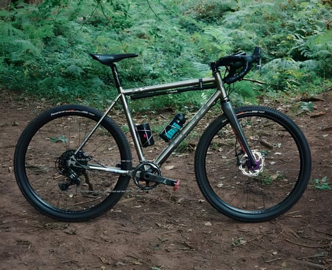 Chris Hunter's titanium Planet X Tempest gravel bike on 650b wheels, parked on a dirt track in woodland.