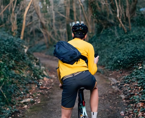 Rider in a yellow top checks a phone with the Chrome Industries Kadet sling bag across their back on a woodland path.