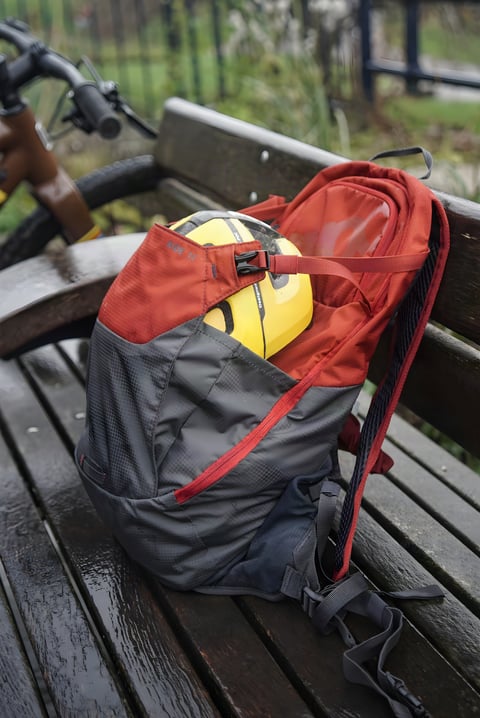 EVOC Ride 12L backpack in red and grey on a wet bench, a yellow helmet in its pouch beside a bike.