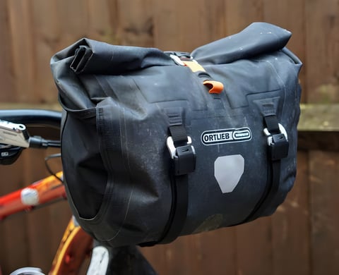Ortlieb Handlebar Pack QR roll-top bar bag, in black with orange tab, fitted to a flat-bar bike.