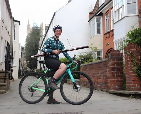 Bassoonist Alison Wormell sits astride her mint green Specialized bike on a town street, holding her bassoon.